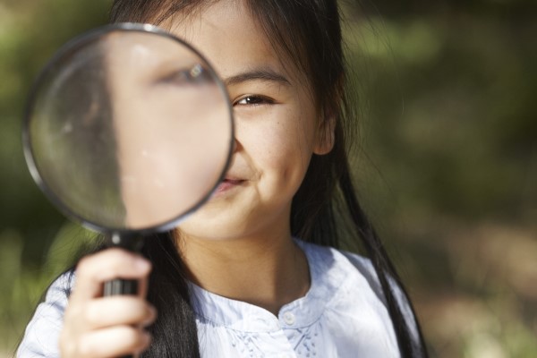 Child looking through a magnifying glass towards the camera.
