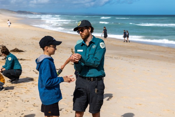 Park ranger and child examining seaweed on a coastal landscape.